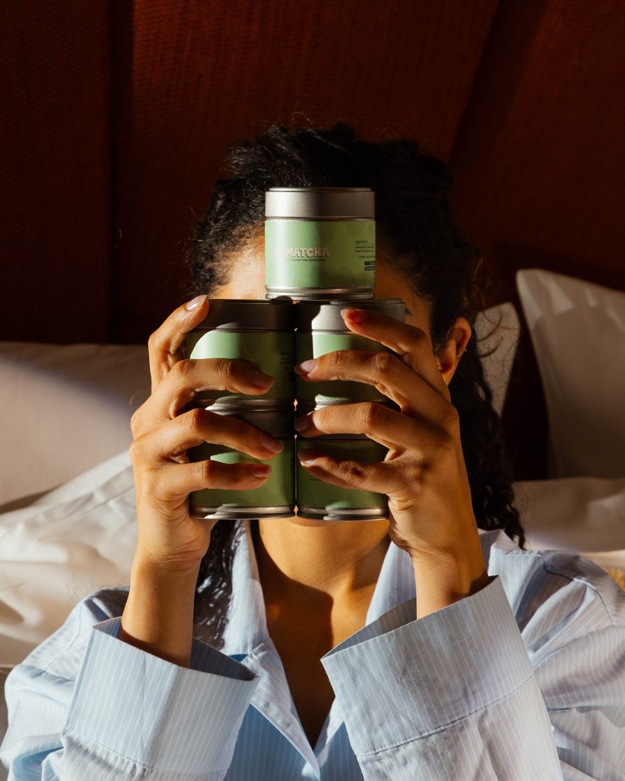 OHMATCHA tins held playfully in front of a face
